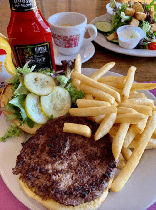 A plate with a burger topped with lettuce and pickles, fries, ketchup, and a side salad in the background.