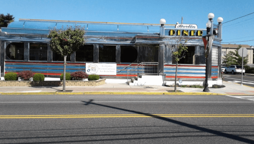 A retro-style diner with a shiny exterior and large windows, located on a busy street.