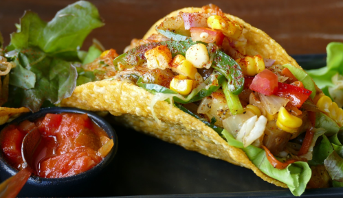A close-up of a taco filled with vegetables, corn, and spices, served with a side of salsa.
