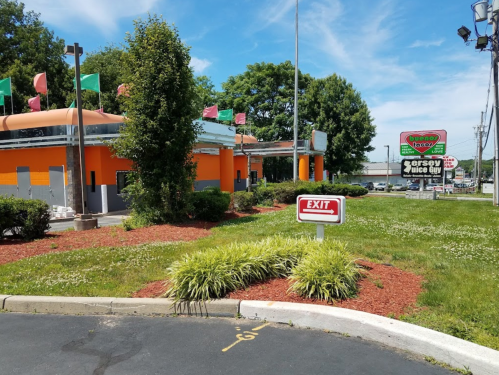 A colorful fast-food restaurant with a large sign, surrounded by green grass and trees, featuring an exit sign.