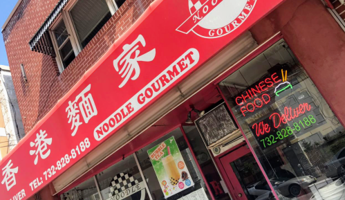 Red storefront of "Noodle Gourmet" with neon signs for Chinese food and delivery, located on a city street.