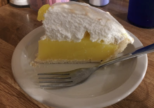 A slice of lemon meringue pie on a plate, featuring a yellow filling and a fluffy white meringue topping.