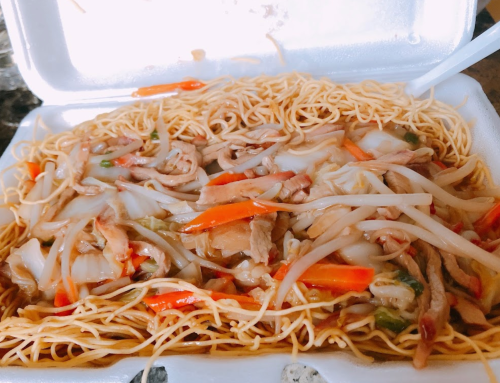 A takeout container filled with stir-fried noodles, vegetables, and sliced meat.