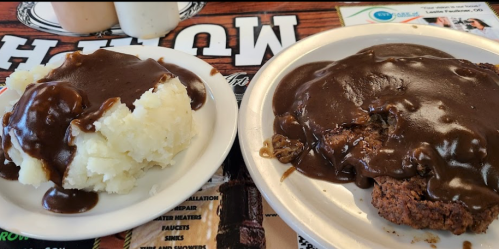 A plate of mashed potatoes and a breaded meat dish smothered in brown gravy, served on a white plate.