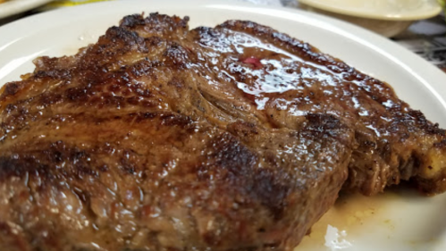 A close-up of a perfectly cooked, juicy steak on a white plate, glistening with juices.