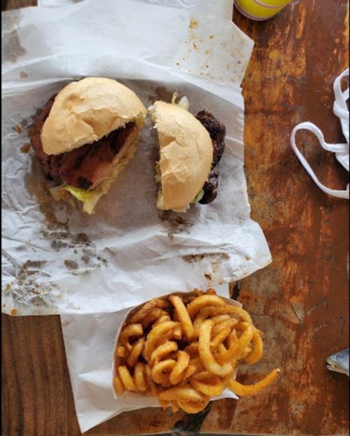 A split sandwich with lettuce and a side of curly fries on a wooden table.
