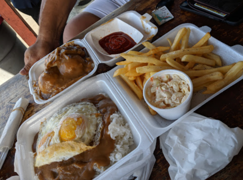 A takeout meal featuring rice with gravy, a fried egg, fries, coleslaw, and a side of ketchup.