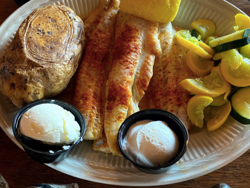 A plate with seasoned fish fillets, a baked potato, sautéed zucchini, and two cups of ice cream.