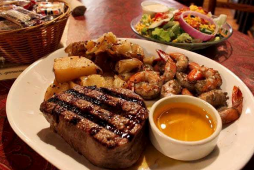 A plate featuring grilled steak, shrimp, seasoned potatoes, and a side salad with dressing.