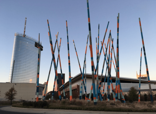 Colorful, tall poles stand in front of a modern glass building against a clear sky during dusk.
