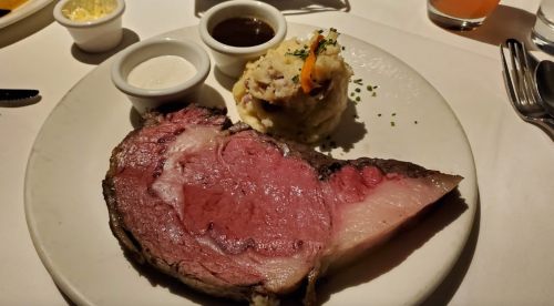A plate featuring a large slice of prime rib, creamy mashed potatoes, and two dipping sauces.