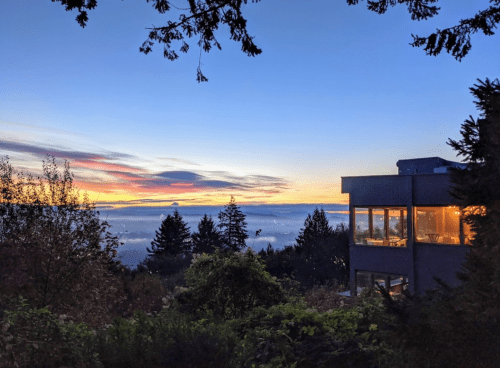 A serene sunset view over misty hills, with a modern house illuminated by warm light in the foreground.