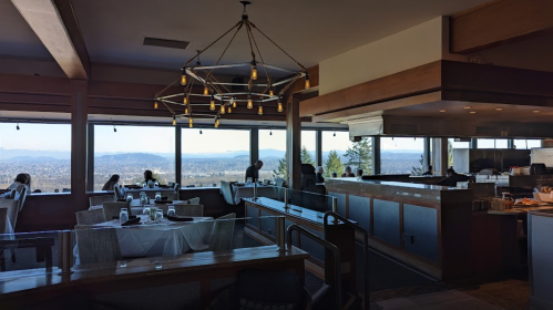 Interior of a restaurant with large windows offering mountain views, featuring tables and a modern chandelier.