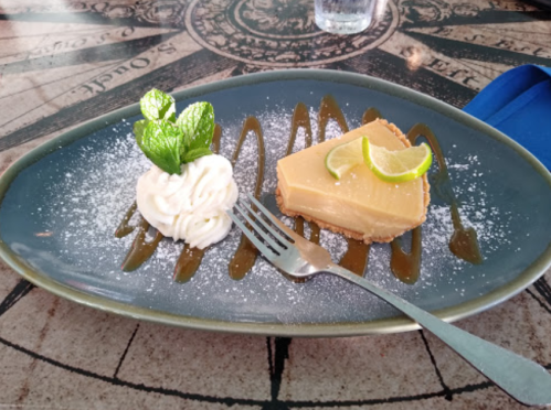 A slice of lime cheesecake with whipped cream and mint, drizzled with caramel sauce on a decorative plate.