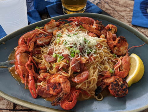 A plate of pasta topped with shrimp, crawfish, and green onions, garnished with cheese and a lemon wedge.