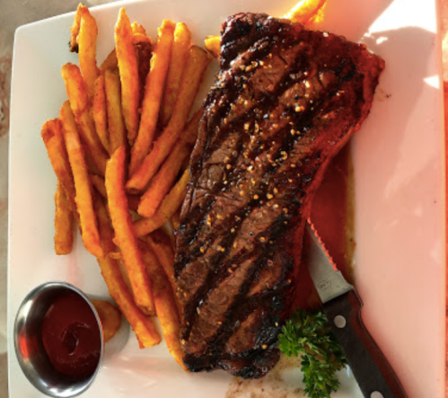 A grilled steak served with golden French fries and a small bowl of ketchup on a white plate.