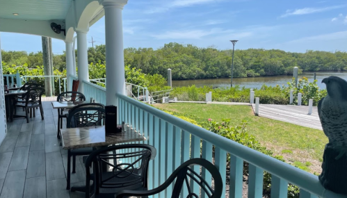 A scenic view from a porch with tables overlooking a lush green area and a calm waterway.