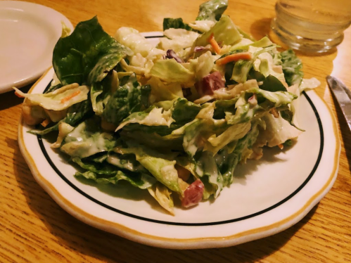 A fresh salad with mixed greens, shredded carrots, and a creamy dressing on a white plate with a black rim.