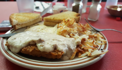 A plate of chicken fried steak topped with gravy, hash browns, toast, and a side of cream.