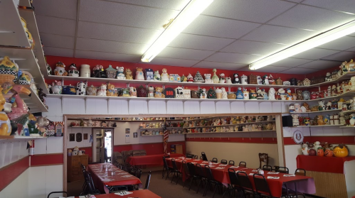 A cozy restaurant interior with red walls, tables, and shelves lined with various decorative ceramic figurines.