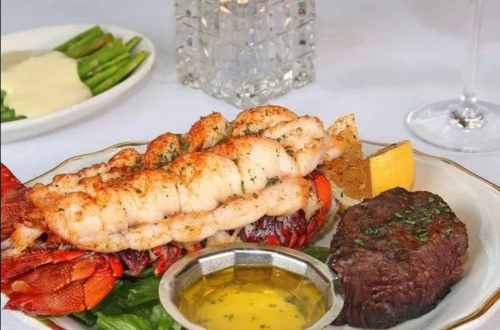 A gourmet plate featuring lobster tail, filet mignon, and a side of melted butter, garnished with lemon and herbs.