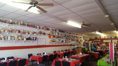 A cozy restaurant with red and green tables, featuring a wall lined with various decorative dolls and figurines.