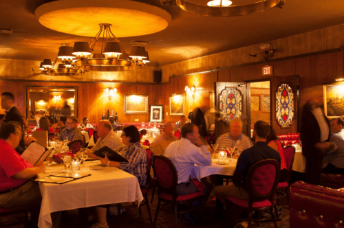 A dimly lit restaurant with wooden decor, patrons dining at tables, and waitstaff moving about.