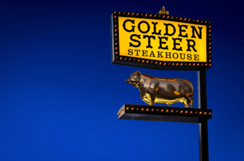 Sign for Golden Steer Steakhouse featuring a lit-up cow figure against a blue sky.