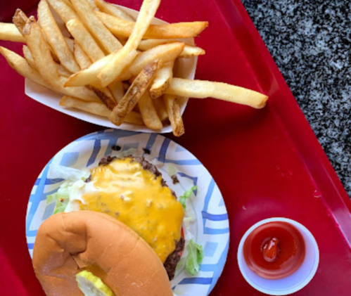 A plate with a cheeseburger, lettuce, and fries, accompanied by a small cup of ketchup on a red tray.