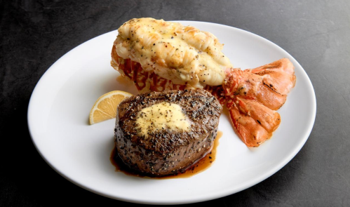 A plate featuring a grilled lobster tail and a filet mignon topped with butter, garnished with a lemon wedge.