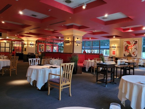 Elegant restaurant interior with red accents, white tablecloths, and modern decor, featuring empty tables and a cozy atmosphere.