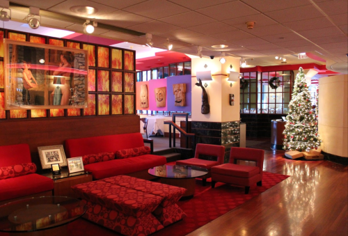 Cozy lounge area with red seating, artwork on the walls, and a decorated Christmas tree in a modern setting.