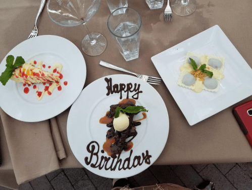 Three dessert plates on a table: a chocolate cake with ice cream, a fruit tart, and a creamy dessert, all celebrating a birthday.