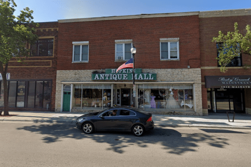 A brick building with a sign reading "Hopkins Antique Mall" and a parked car in front on a sunny day.