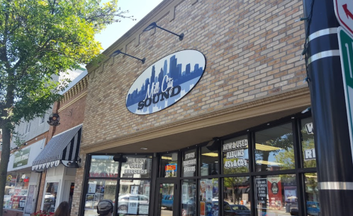 Storefront of "Music Sound" with a city skyline logo, featuring large windows displaying records and music items.