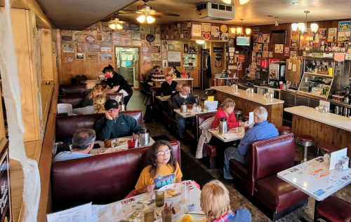 A cozy diner interior with patrons seated in booths, enjoying meals amidst vintage decor and a bustling atmosphere.