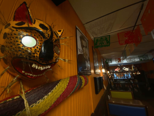 Colorful mask on an orange wall, with a poster and festive decorations in a cozy restaurant setting.
