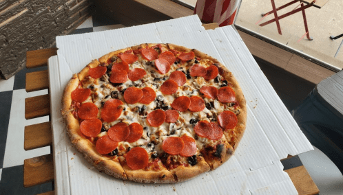 A large pepperoni pizza with melted cheese and black olives on a white pizza box, set on a wooden table.