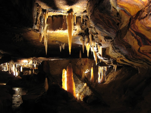 Stalactites and stalagmites in a dimly lit cave, showcasing intricate rock formations and natural lighting.