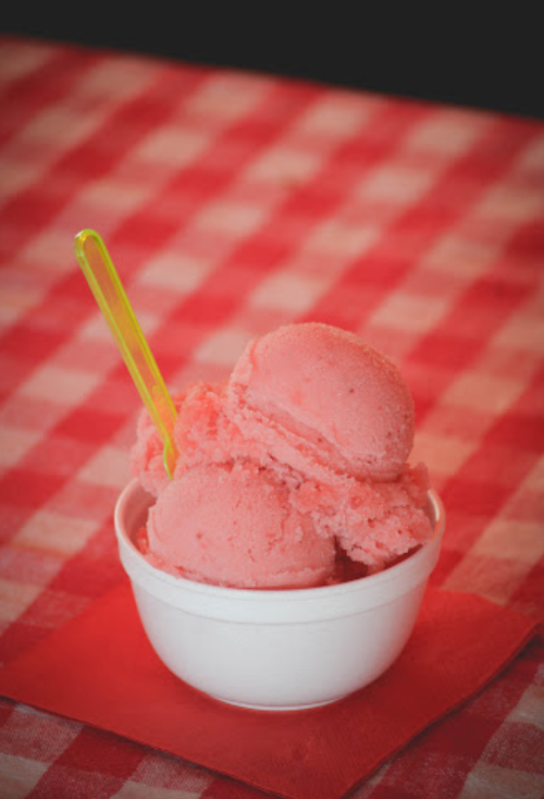 A bowl of pink sorbet with a yellow spoon, placed on a red and white checkered tablecloth.