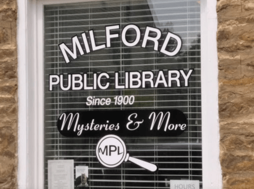 Sign on a window reading "Milford Public Library" with "Since 1900" and "Mysteries & More" below.
