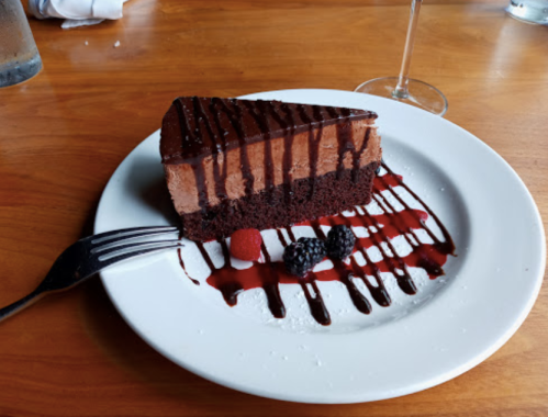 A slice of chocolate mousse cake drizzled with chocolate sauce, served with raspberries and blackberries on a white plate.