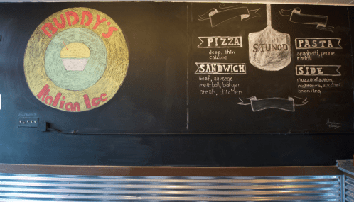 Chalkboard menu at Buddy's Italian Ice featuring pizza, sandwiches, pasta, and sides with colorful illustrations.