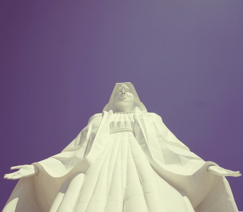 A towering white statue of a figure with outstretched arms against a clear blue sky.
