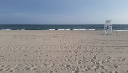 A sandy beach with gentle waves and a lifeguard chair in the distance under a clear blue sky.