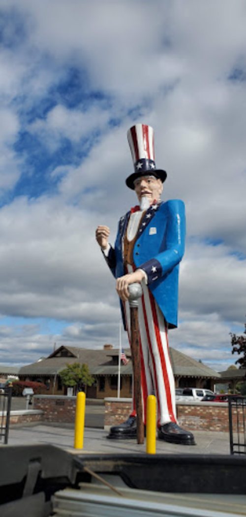 A large statue of Uncle Sam in a patriotic outfit stands in front of a building under a cloudy sky.