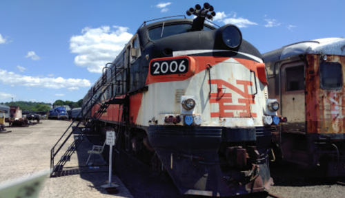 A vintage train engine, numbered 2006, parked in a rail yard under a blue sky with fluffy clouds.