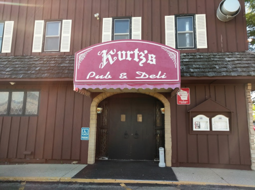 Sign for Kurtz's Pub & Deli on a brown wooden building with white shutters and a stone archway entrance.