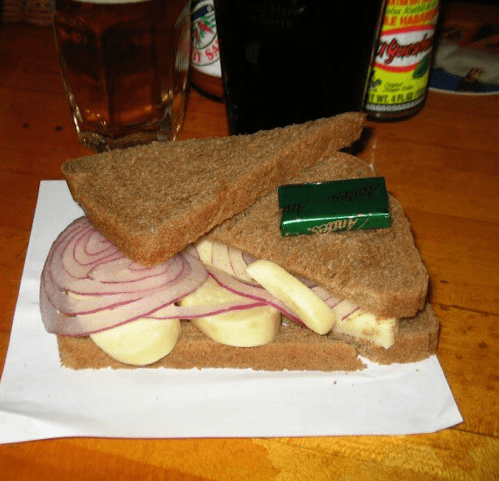 A sandwich made with dark bread, sliced onions, cheese, and a small packet of butter, placed on a napkin.