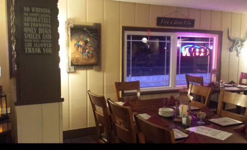 Cozy restaurant interior with wooden tables, chairs, and a colorful artwork on the wall, featuring a neon sign.